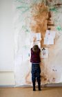 Мальчик приклеивает бумагу к стене — стоковое фото