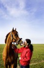 Vista lateral de la mujer besar caballo en el campo bajo cielo despejado - foto de stock