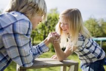 Siblings arm wrestling on wooden table in back yard — Stock Photo