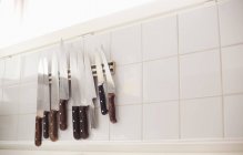 Various knives on tiled wall — Stock Photo