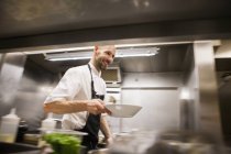 Шеф-повар держит блюдо во время прогулки на кухне — стоковое фото