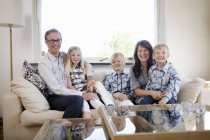 Família com três crianças sentadas no sofá em casa interior — Fotografia de Stock