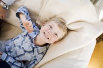 Visão aérea do menino sorridente deitado no sofá em casa — Fotografia de Stock