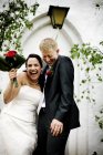 Recém-casados alegres em pé contra a construção e rindo — Fotografia de Stock