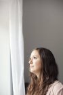Frau steht zu Hause vor Vorhang — Stockfoto