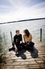 Мати розмовляє з дочкою на пірсі над озером в сонячний день — стокове фото