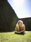 Вид спереди девочки-подростка, читающей книгу на траве в парке — стоковое фото