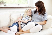 Mother and daughter lying together on sofa at home — Stock Photo
