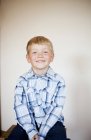 Lächelnder blonder Junge sitzt zu Hause gegen Wand — Stockfoto