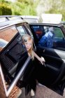 Mädchen blickt durch geöffnete Autotür mit Bruder im Hintergrund — Stockfoto
