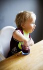 Niño jugando con la bebida en el vaso en la mesa - foto de stock