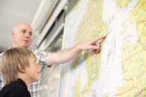 Low angle view of male teacher explaining map to boy in classroom — Stock Photo