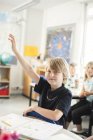 Écolier levant la main dans la salle de classe — Photo de stock