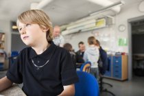 Thoughtful schoolboy sitting in classroom — Stock Photo