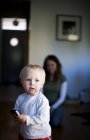 Kleiner blonder Junge mit Mutter im Hintergrund im Zimmer — Stockfoto