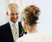 Novio sonriente mirando a la novia durante la boda - foto de stock