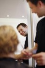 Крупним планом усміхнений чоловічий перукар, що ріже впізнаване волосся людини в салоні — стокове фото
