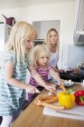Daughter cutting sausages in kitchen — Stock Photo