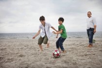 Fils jouant au soccer à la plage — Photo de stock