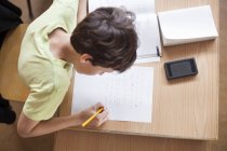 Хлопчик пише на папері за столом — стокове фото