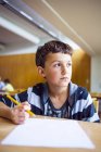 Thoughtful schoolboy sitting at desk — Stock Photo