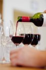 Mains versant du vin rouge dans un verre — Photo de stock