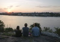 Persone sedute vicino al fiume al tramonto — Foto stock