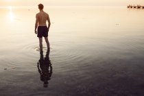 Mann in kurzen Hosen watet bei Sonnenuntergang im Meer — Stockfoto