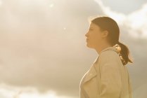 Вид сбоку женщины, стоящей на фоне неба в мягком свете — стоковое фото