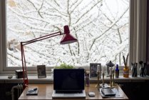 Лампа и ноутбук на столе за окном — стоковое фото