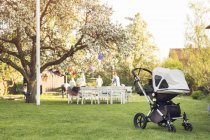Baby carriage in garden with people in the background — Stock Photo