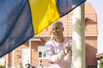 Mature man raising Swedish flag in back yard — Stock Photo