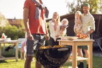 Family with children watching man at barbecue grill — Stock Photo