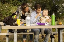 Family sitting by picnic table — Stock Photo