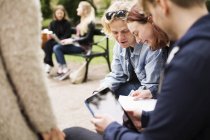 Grupo de estudiantes sentados y conversando en patio universitario con tablet digital - foto de stock