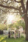Семья сидит за обеденным столом на вечеринке в саду на заднем дворе — стоковое фото