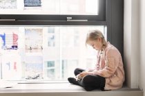 Girl sitting on window sill with smartphone — Stock Photo