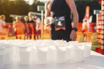 Стол с чашками воды на спортивном мероприятии с неузнаваемым фоном — стоковое фото