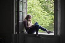 Estudiante sentada en alféizar de ventana con tableta digital - foto de stock