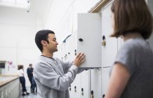 Two students talking in front of open locker with unrecognizable people in background — Stock Photo
