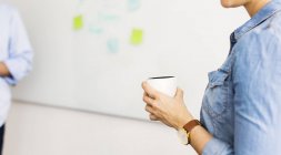 Cropped view of woman holding cup in front of whiteboard — Stock Photo