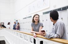 Two students standing with coffee by railing in front of lockers — Stock Photo