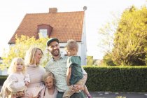 Familia con tres niños de pie frente a casa suburbana - foto de stock