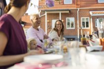 Семья сидит за обеденным столом на вечеринке в саду на заднем дворе — стоковое фото