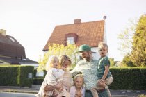 Familia con tres niños de pie frente a casa suburbana - foto de stock