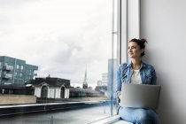 Woman with laptop looking through window in office — Stock Photo