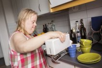Mulher com síndrome de down derramando leite para caneca na cozinha — Fotografia de Stock