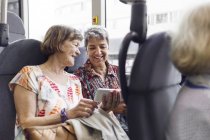 Дві усміхнені жінки дивляться на мобільний телефон в автобусі — стокове фото