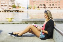 Молода жінка читає книгу, сидячи на вулиці — стокове фото