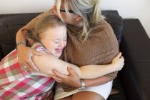 Мать и дочь с синдромом Дауна обнимаются на диване — стоковое фото